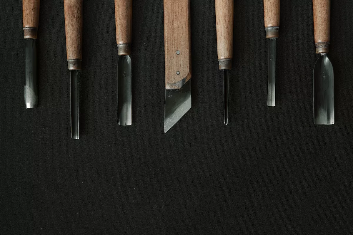various wood carving tools sit on a black table cloth.