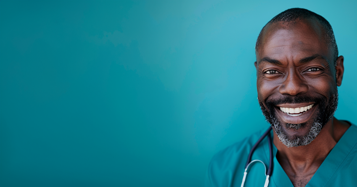 A male physician in scrubs with a sthescope around his neck smiles at the camera against a bright turquoise background.